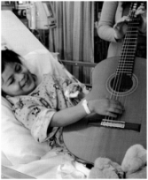 Music_Heals Hospitalized child beams with joy as she helps a musician play a guitar